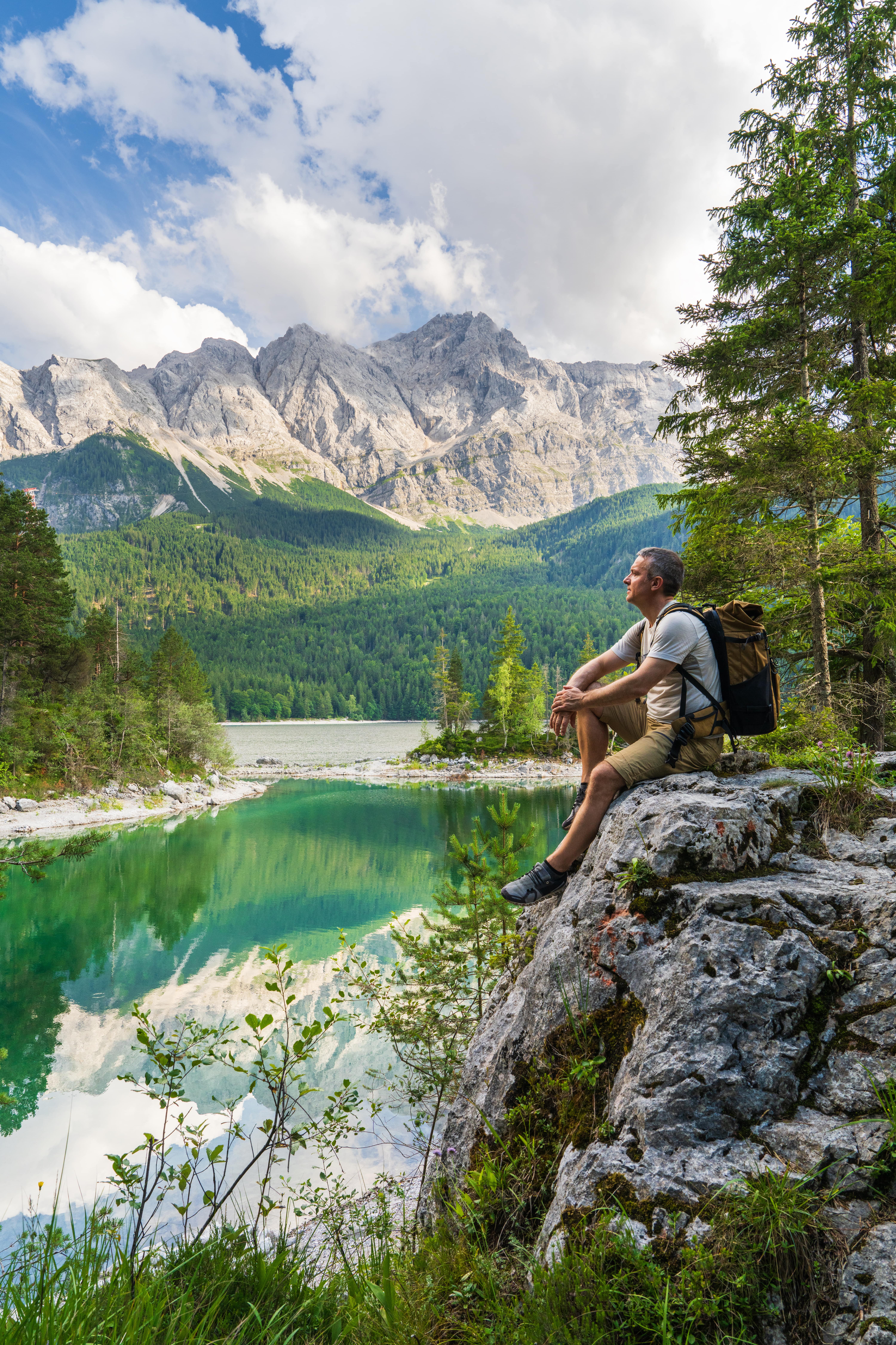 A hiker sitting on a large rock formation with a scenic mountain view in the background.
