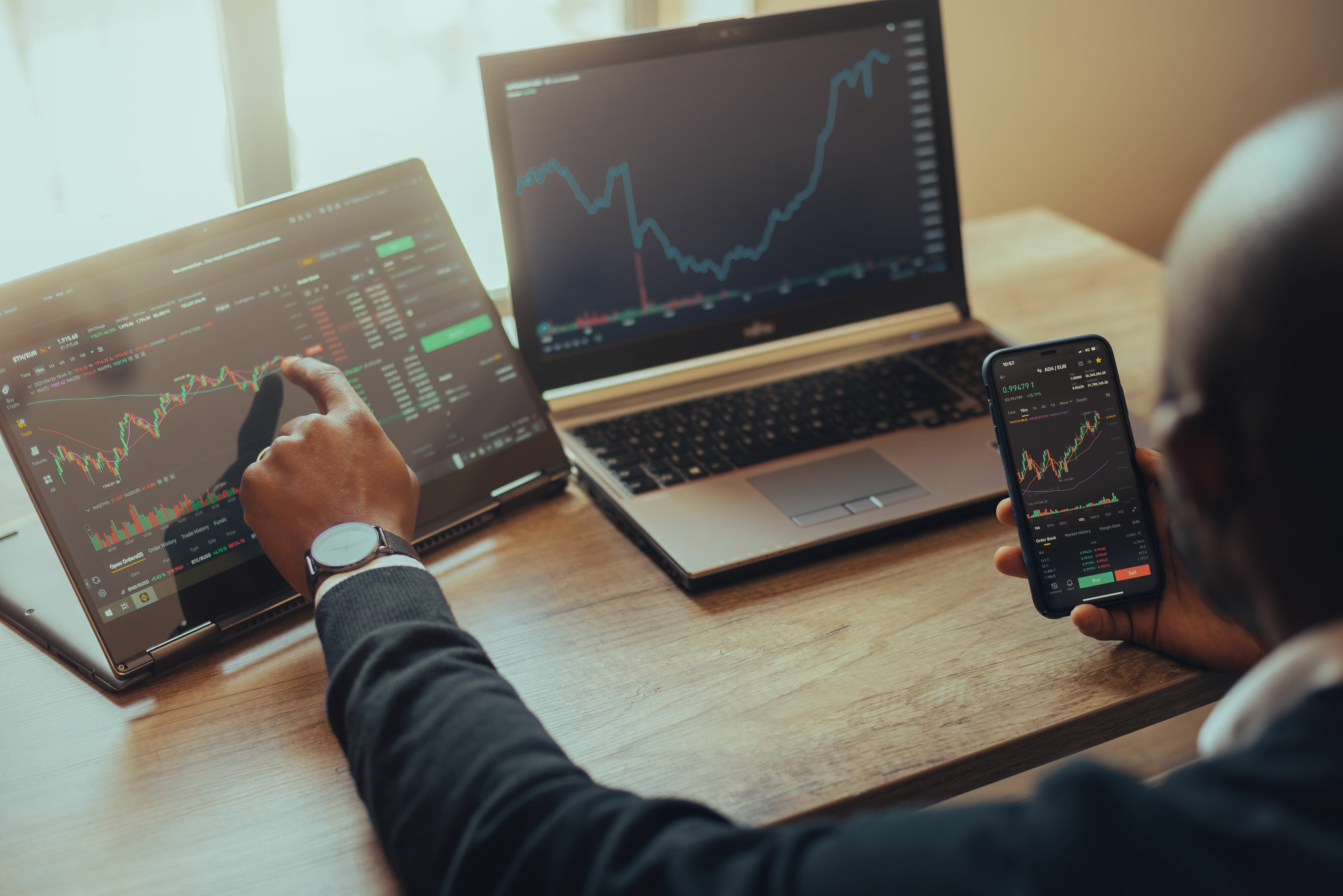 Over the shoulder view of a man at his desk trading on multiple devices.